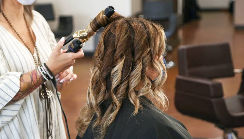 Pracownica w salonie fryzjerskim robi kobiecie loki które nie niszczą włosów